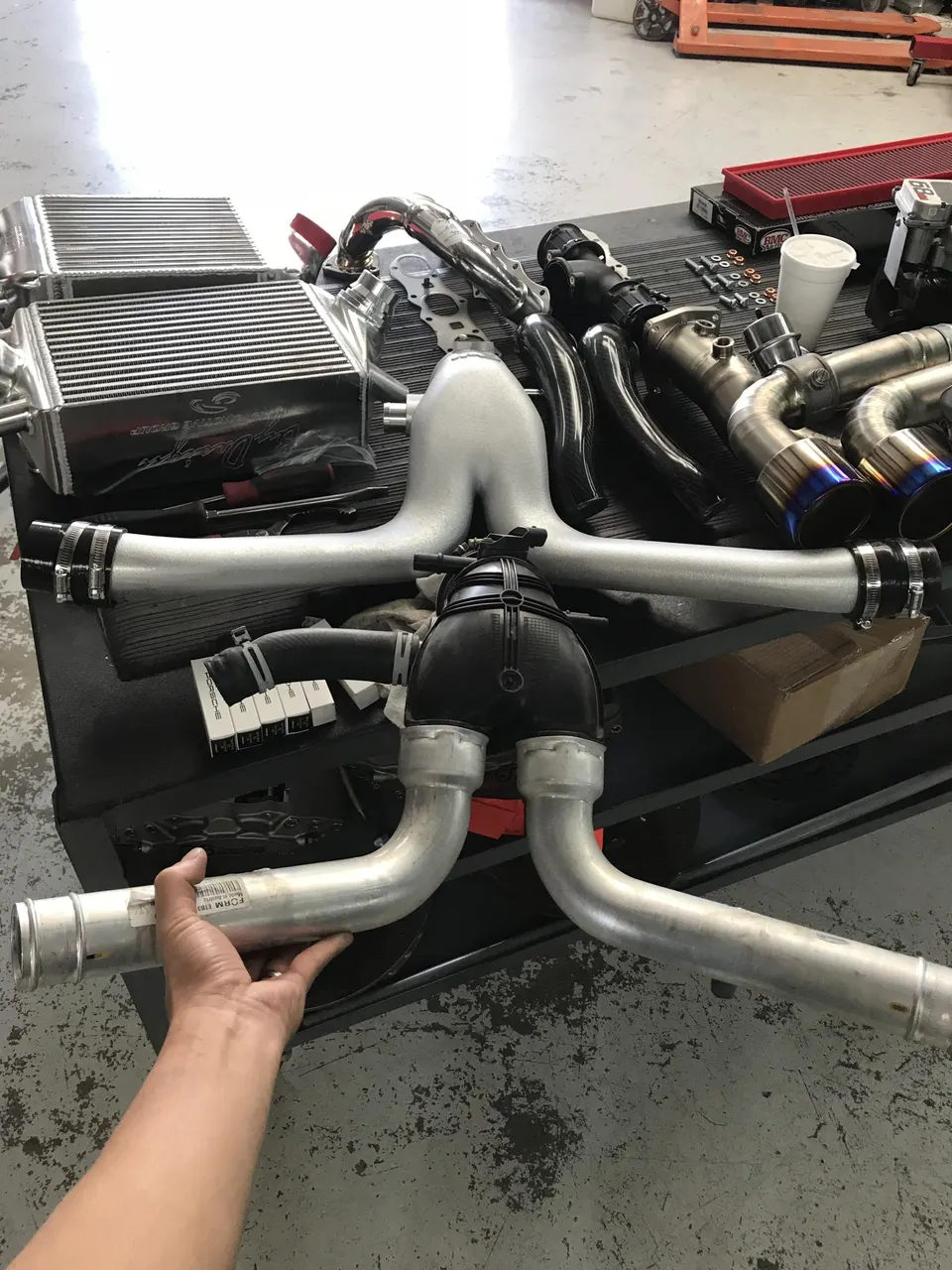 Performance car parts including intercoolers, boost pipes, and exhaust components on a shop workbench.