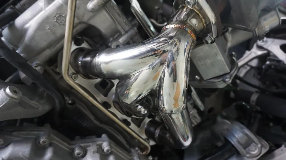 A close-up of a polished aftermarket exhaust header installed in an engine bay.