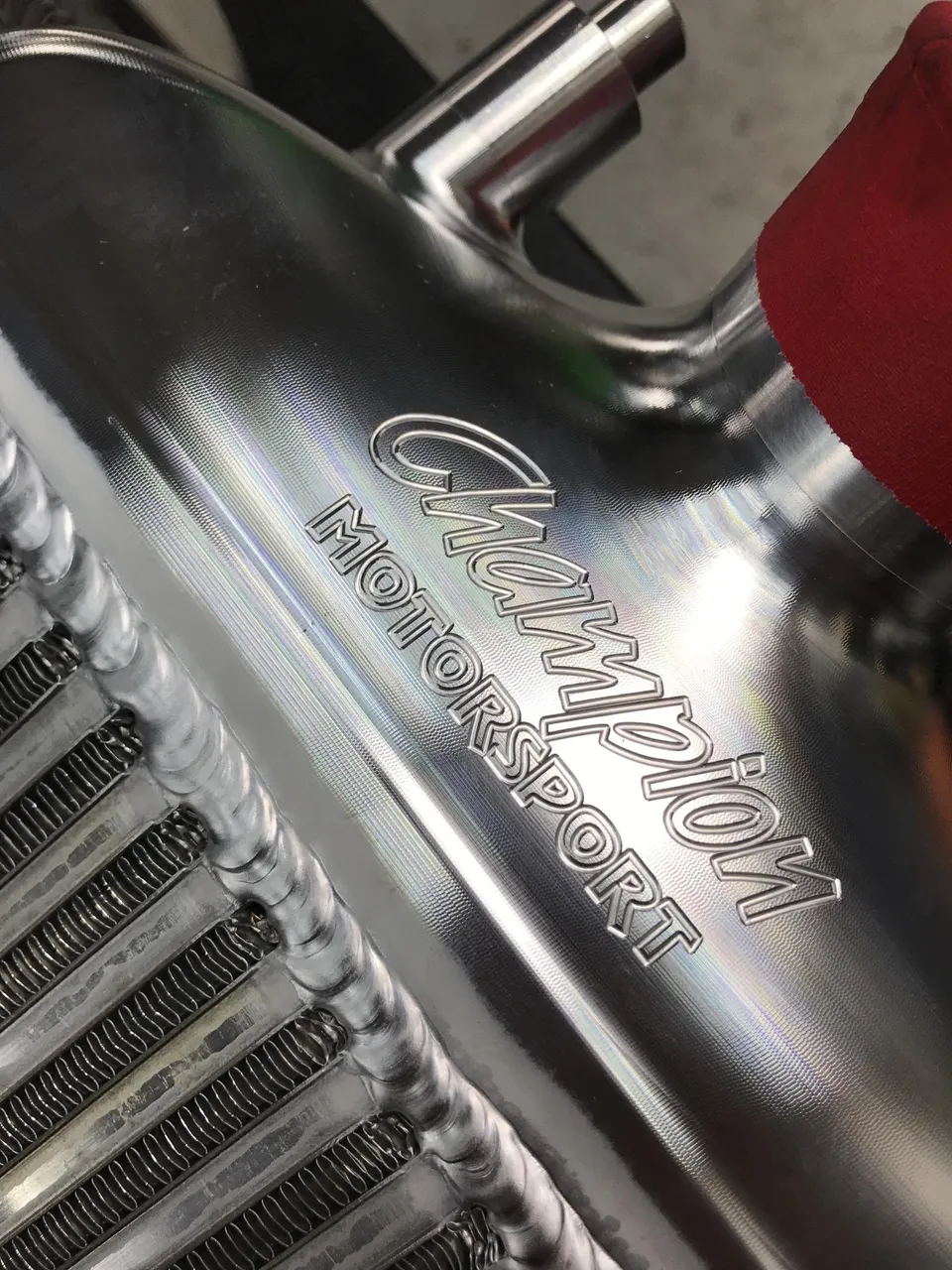 Close-up of a Champion Motorsport aluminum intercooler with visible welds and a red silicone coupler.