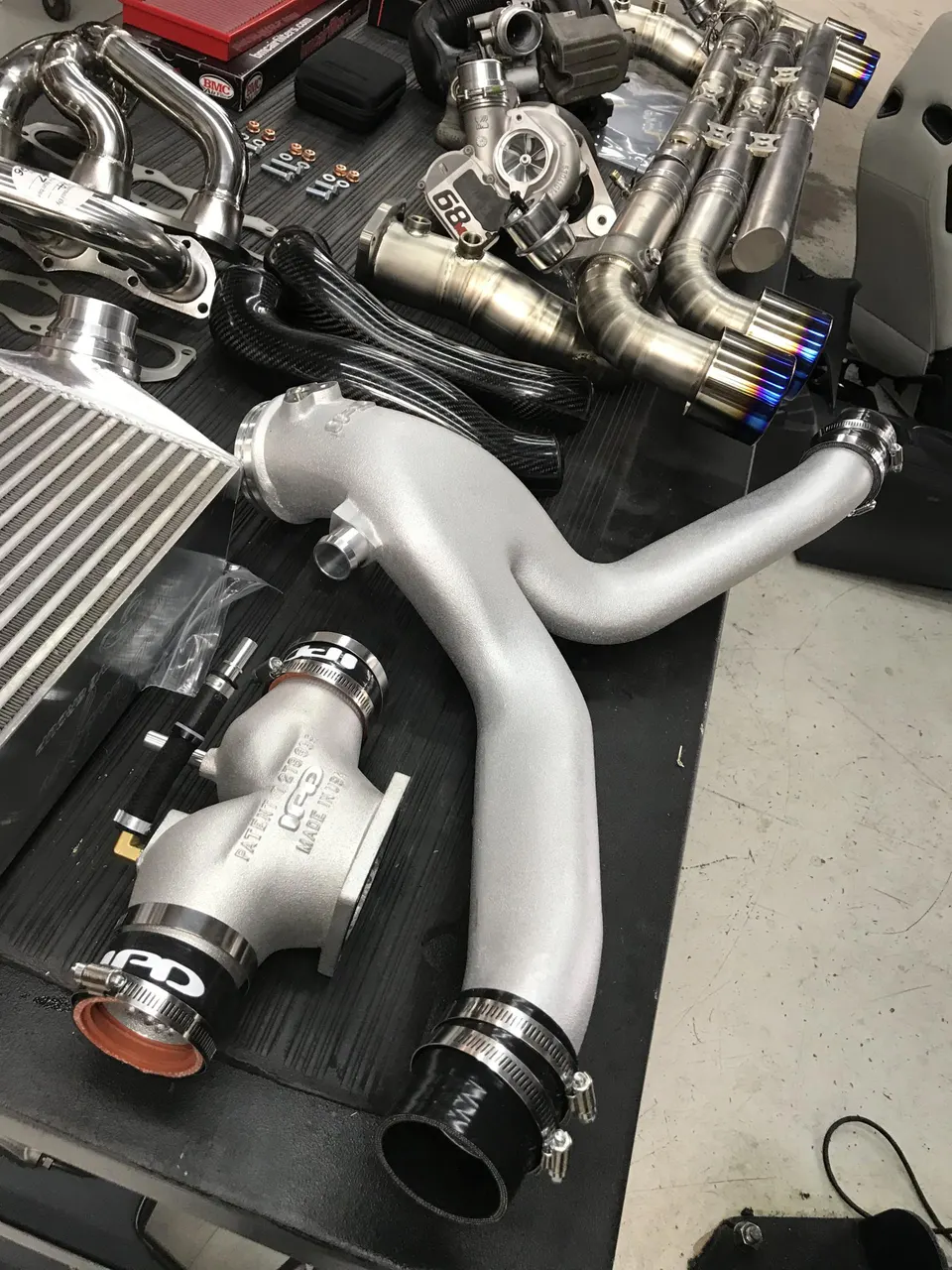 A collection of high-performance turbochargers, exhaust systems, intercooler, and carbon fiber boost pipes on a workbench.