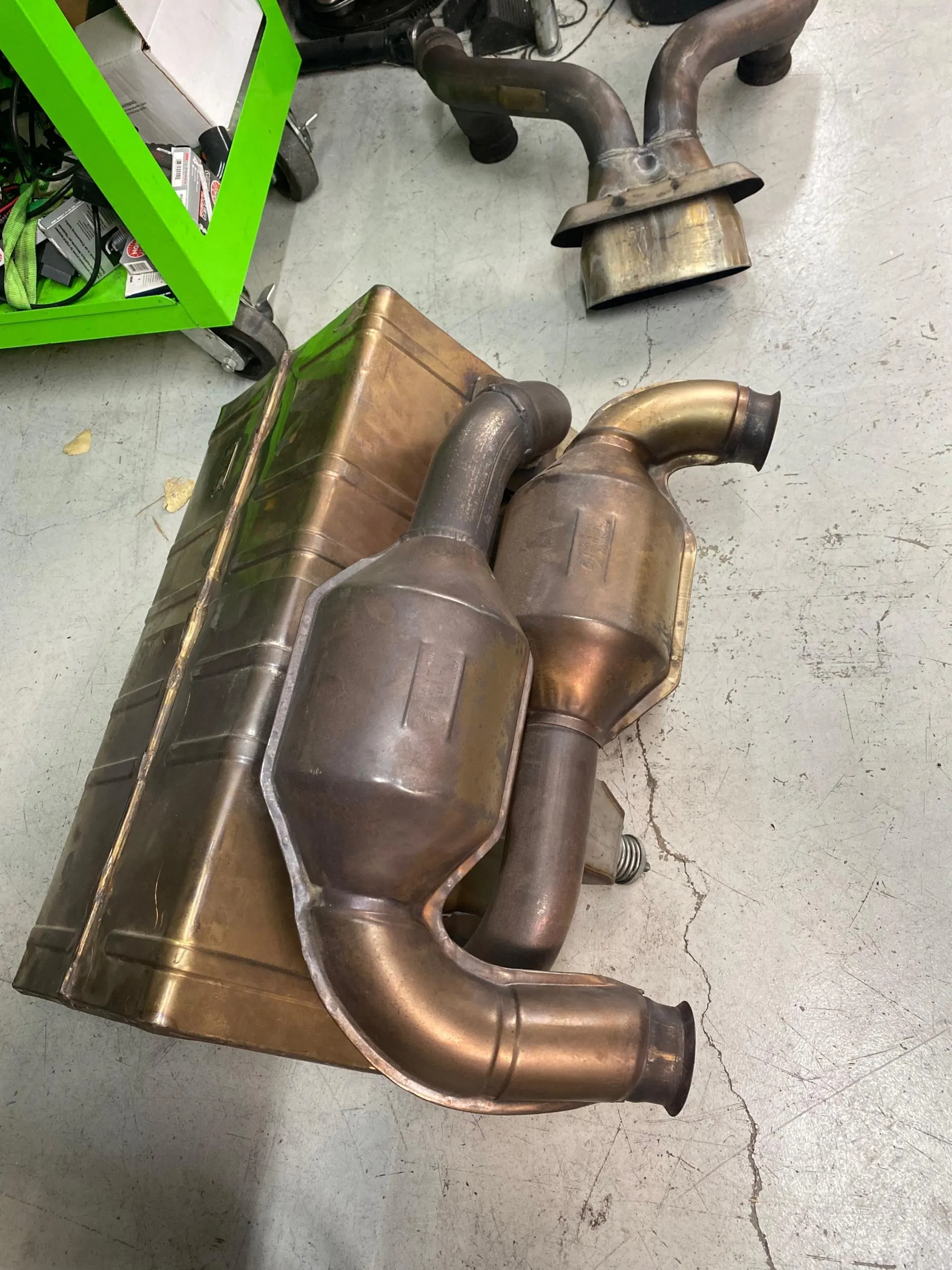 Used catalytic converters and exhaust components on a concrete floor in an automotive shop