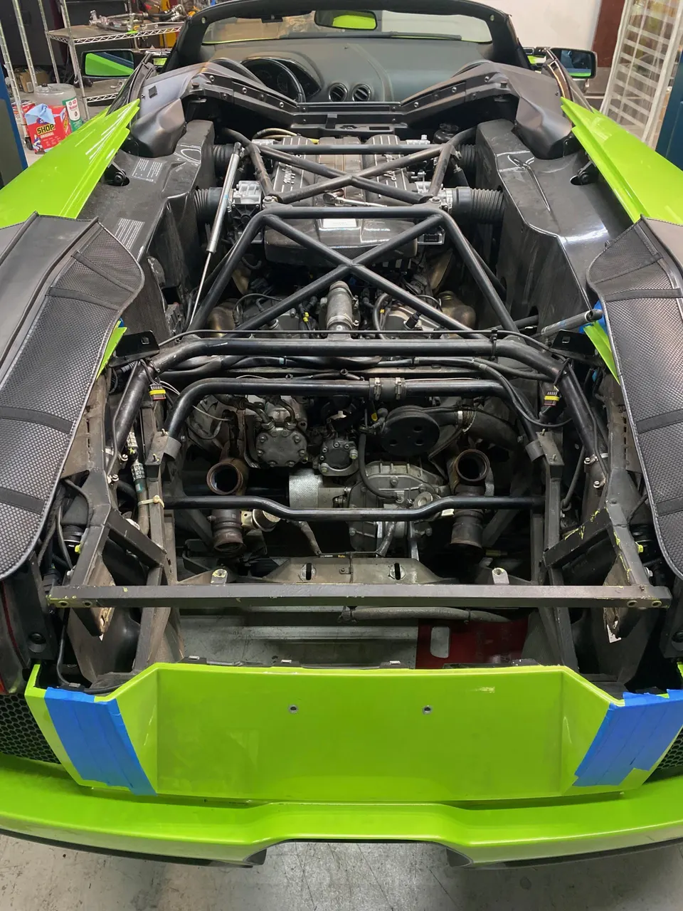 A Lamborghini with its rear bodywork removed, exposing the engine bay with a twin-turbo setup in a performance shop.