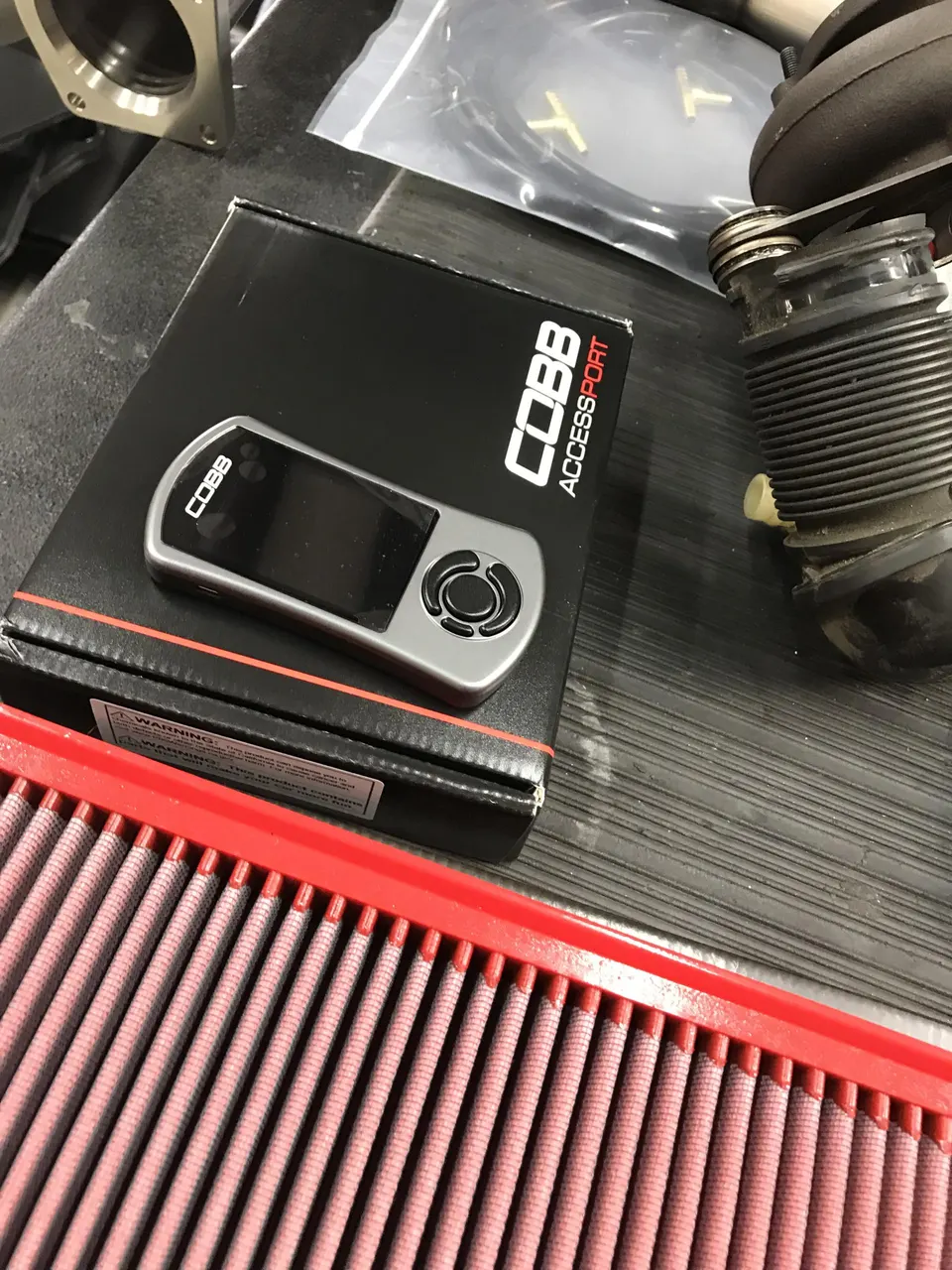 COBB Accessport tuning device, red air filter, and other performance parts laid out on a shop bench.