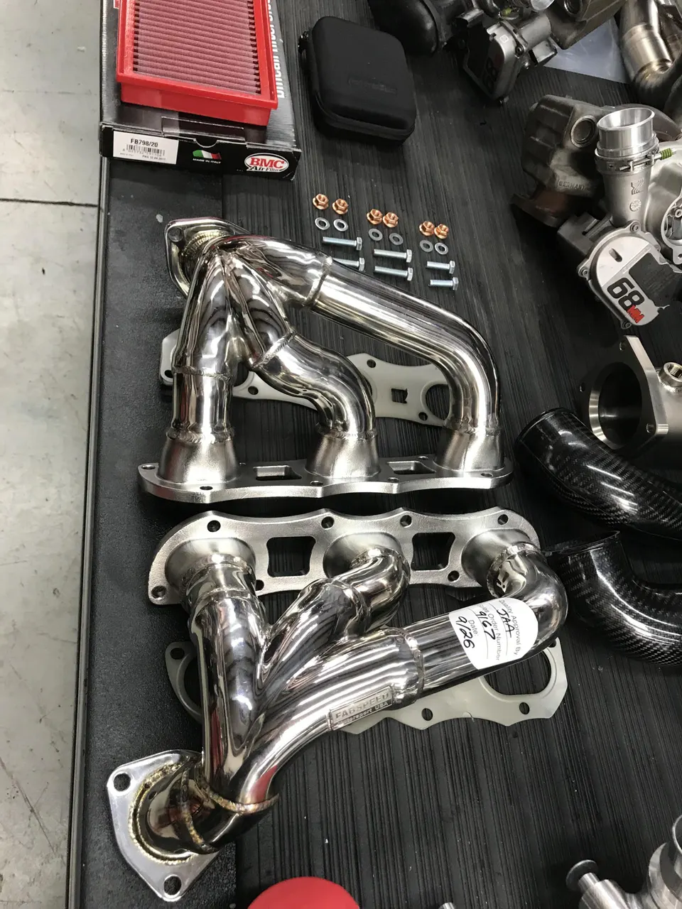 Performance exhaust headers and an air filter laid out on a workbench in a tuning shop.