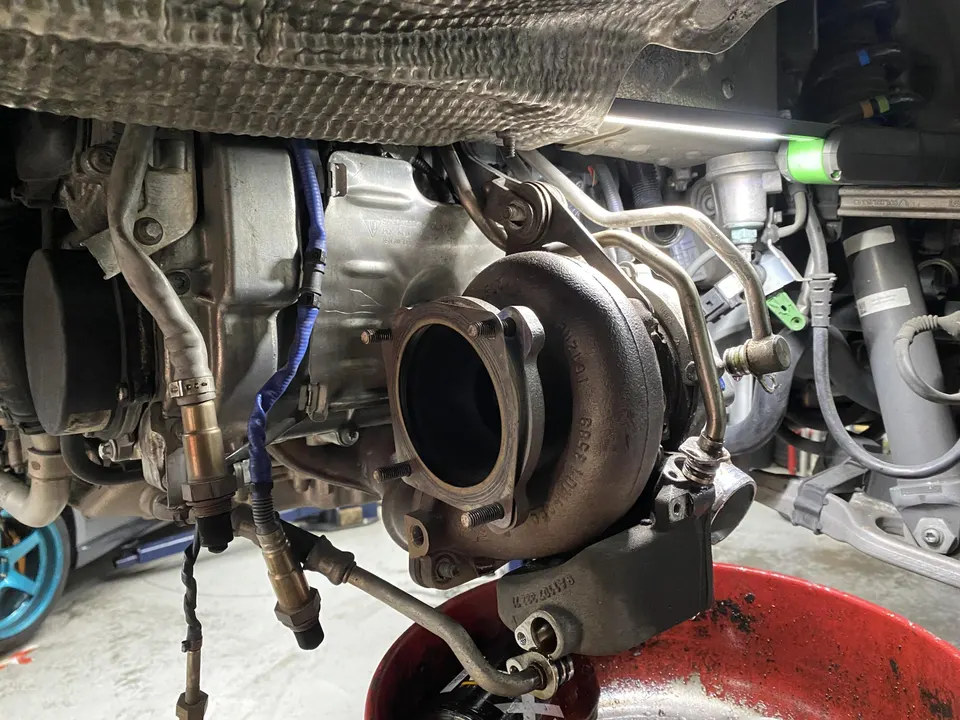 Close-up view of a turbocharger and exhaust components under a car during service at a performance shop.