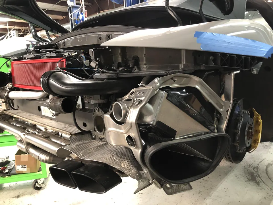 Rear view of a Porsche 911 undergoing performance upgrades in a shop, showcasing aftermarket exhaust, intake, and intercooler.