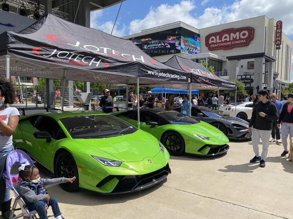 Lime green Lamborghini Huracan and other supercars displayed under Jotech Motorsports tents at an outdoor car event.