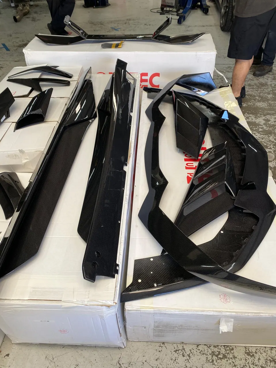 Various carbon fiber exterior aero parts laid out on boxes in a performance tuning shop, ready for installation.