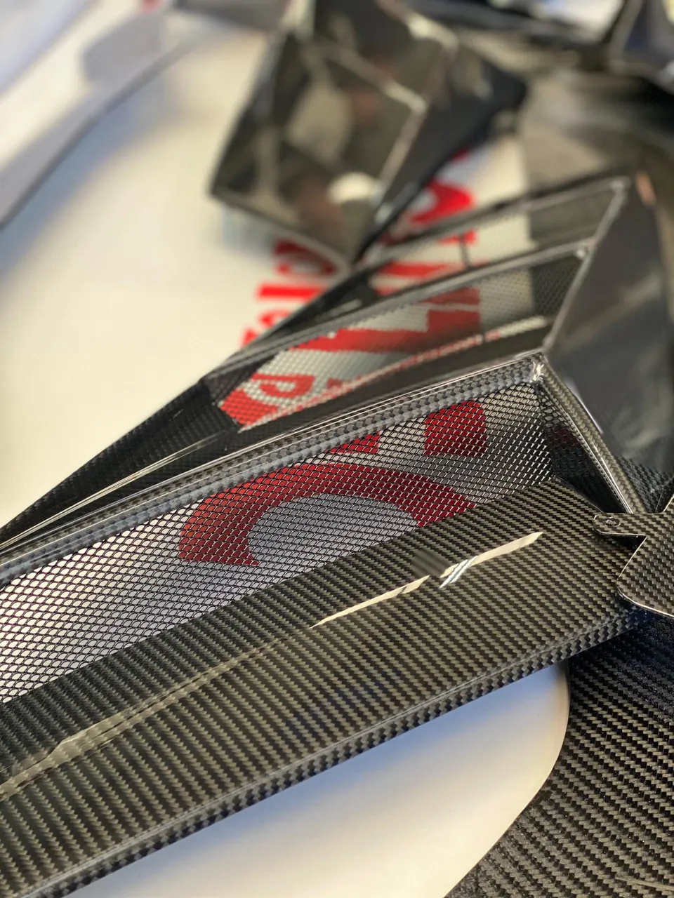 Close-up of multiple carbon fiber aerodynamic parts with mesh details, showcasing the weave and design.