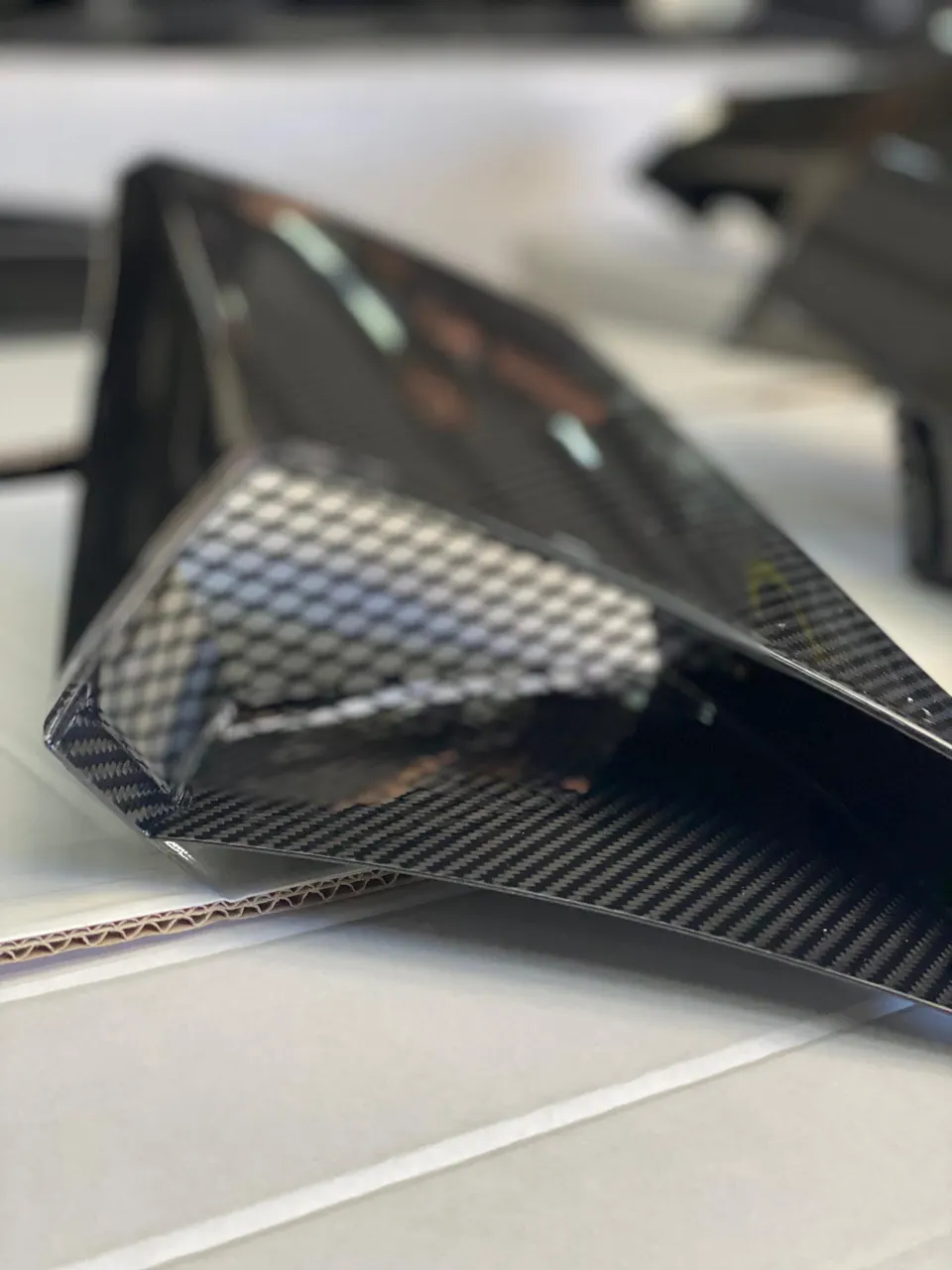 Close-up of a glossy carbon fiber aerodynamic car part, showcasing the intricate weave pattern and reflective surface.