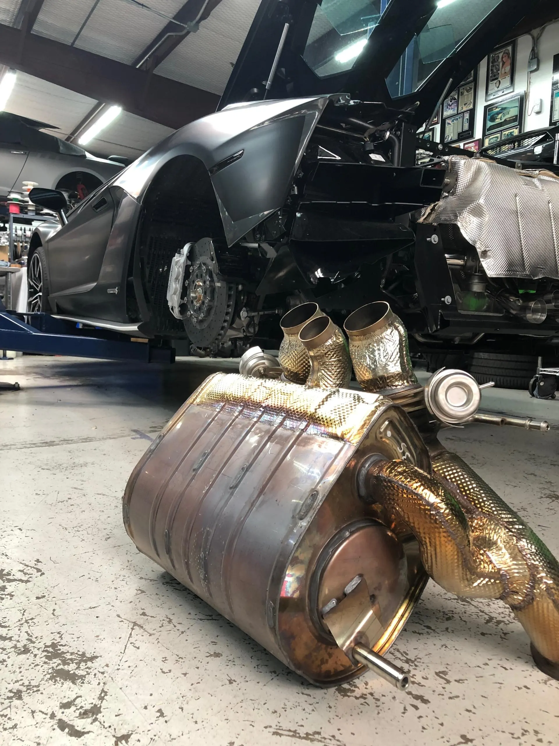Lamborghini Aventador in a shop with its exhaust system removed and laid on the floor for service or upgrade.