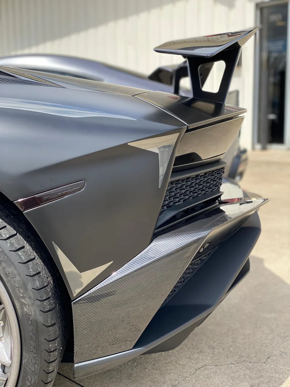 A matte black Lamborghini Aventador with a large carbon fiber rear wing and diffuser.