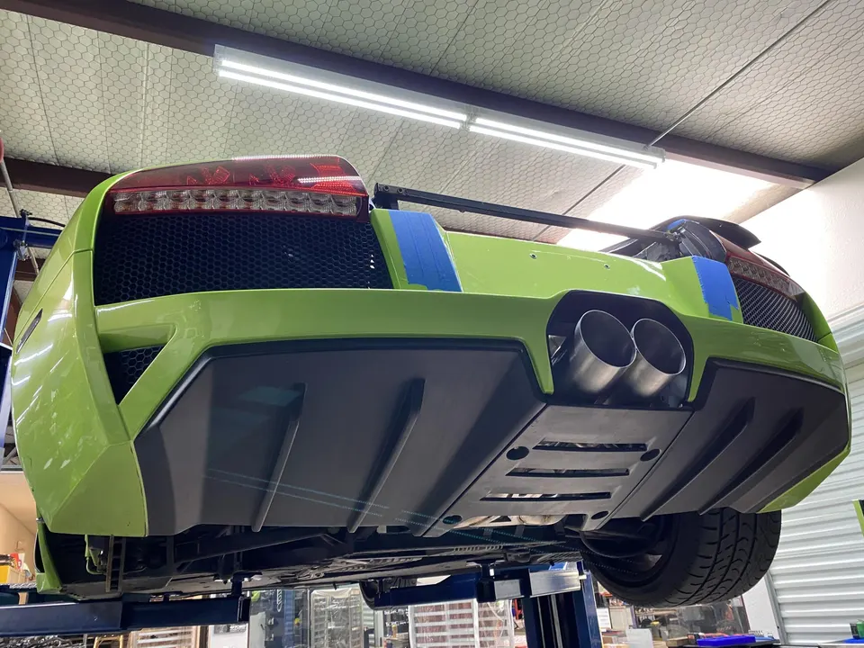 Rear view of a green Lamborghini Murcielago on a lift in a performance shop, showcasing its exhaust and diffuser.