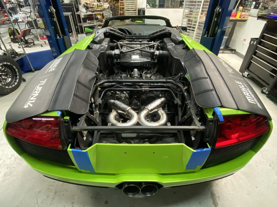 Lime green Lamborghini Murcielago in a shop with its engine bay open, showcasing custom exhaust headers.