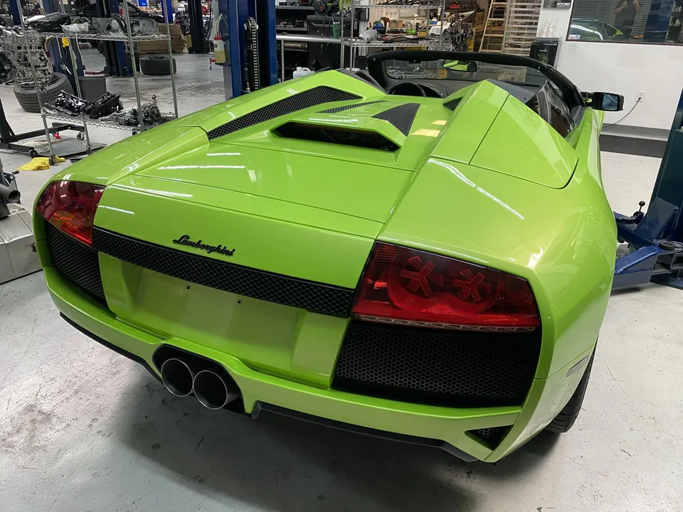 Rear view of a bright green Lamborghini Murcielago convertible in a performance tuning shop, showcasing its dual exhaust.
