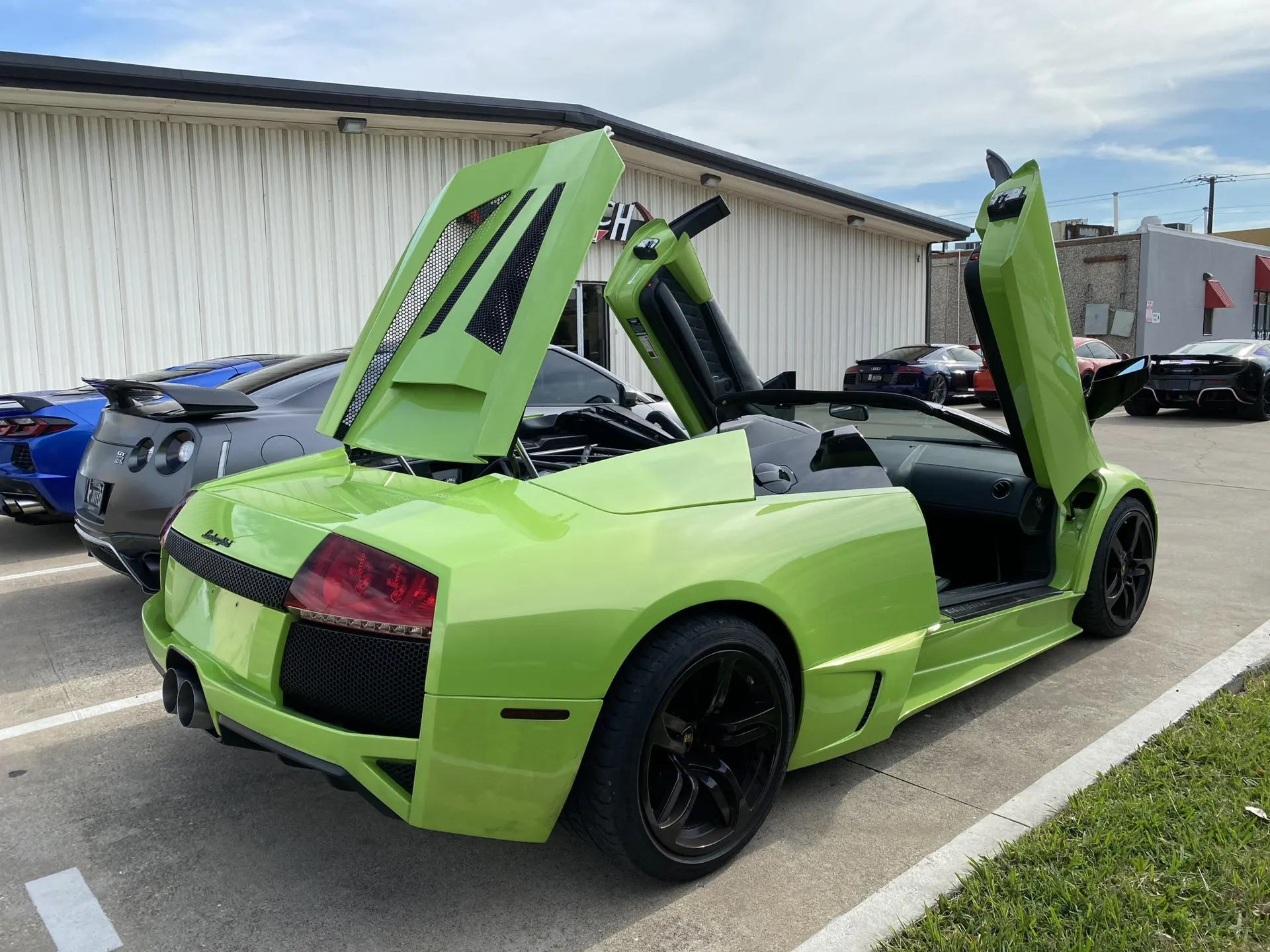 A vibrant green Lamborghini Murcielago with its iconic scissor doors and engine cover open, parked outside a building.
