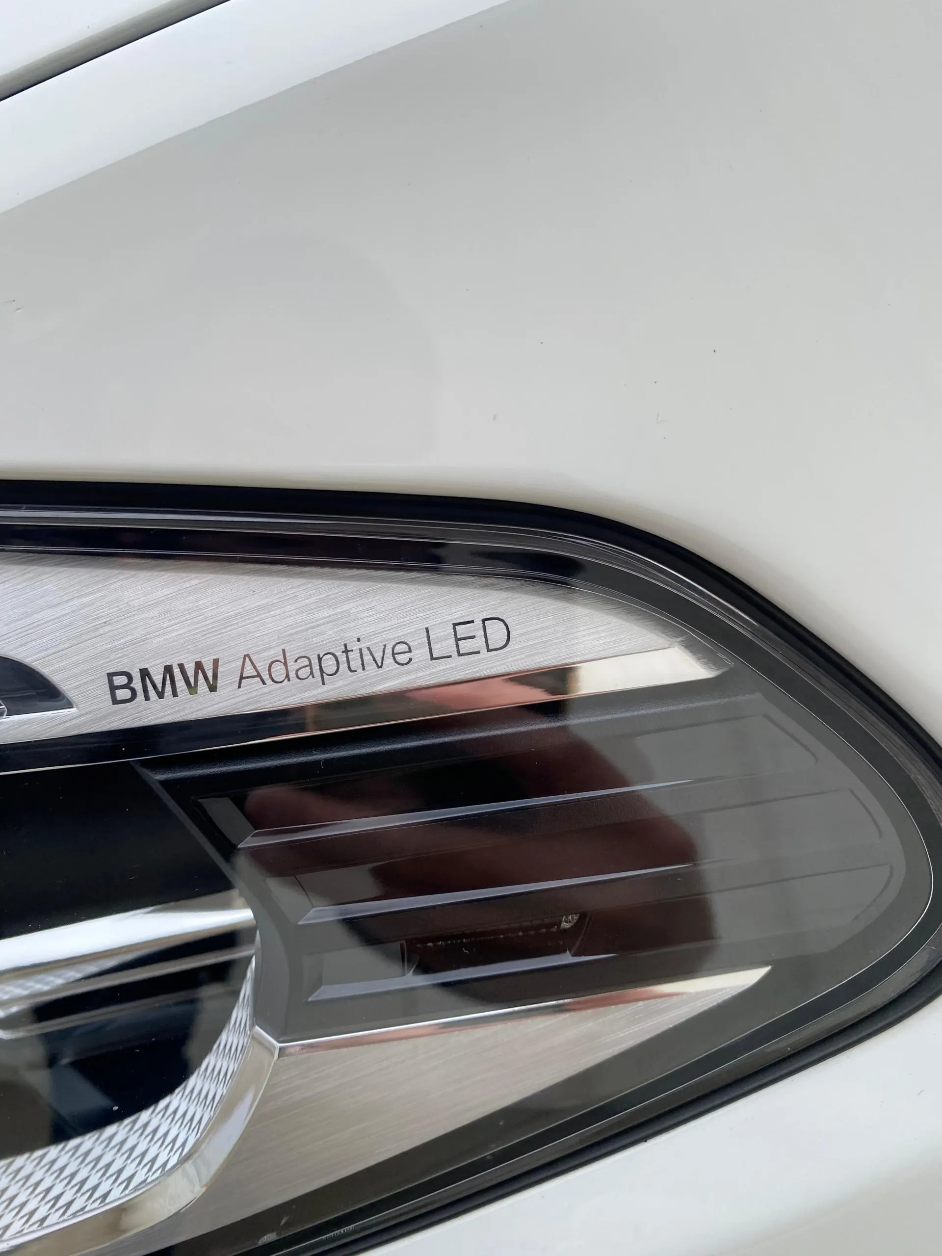 Close-up of a BMW Adaptive LED headlight on a white car, showing the etched text on the light housing.