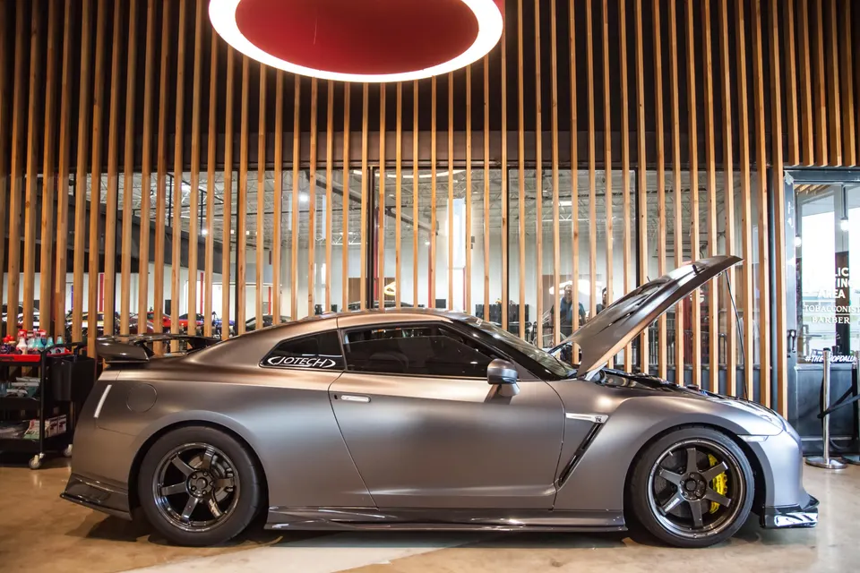 Matte grey Nissan GT-R with its hood open, parked inside a Jotech Motorsports showroom with wooden slat walls.