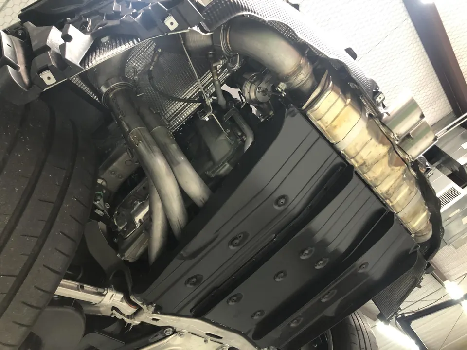 Underside view of a performance car showing custom exhaust system, downpipes, and heat shielding in a shop.