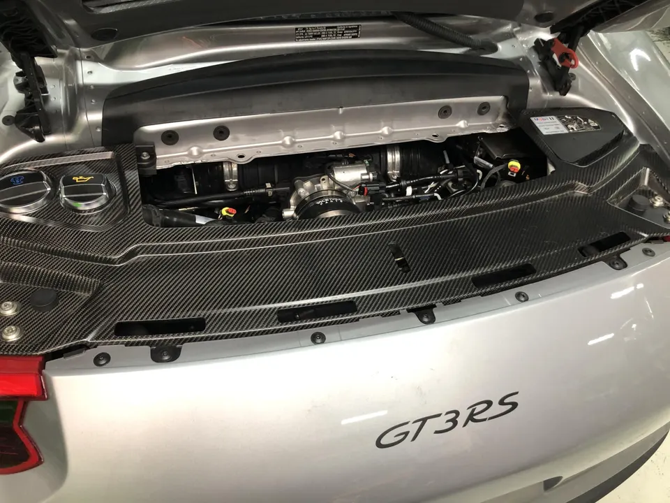 A close-up view of the Porsche GT3RS engine bay with carbon fiber trim and visible induction components.
