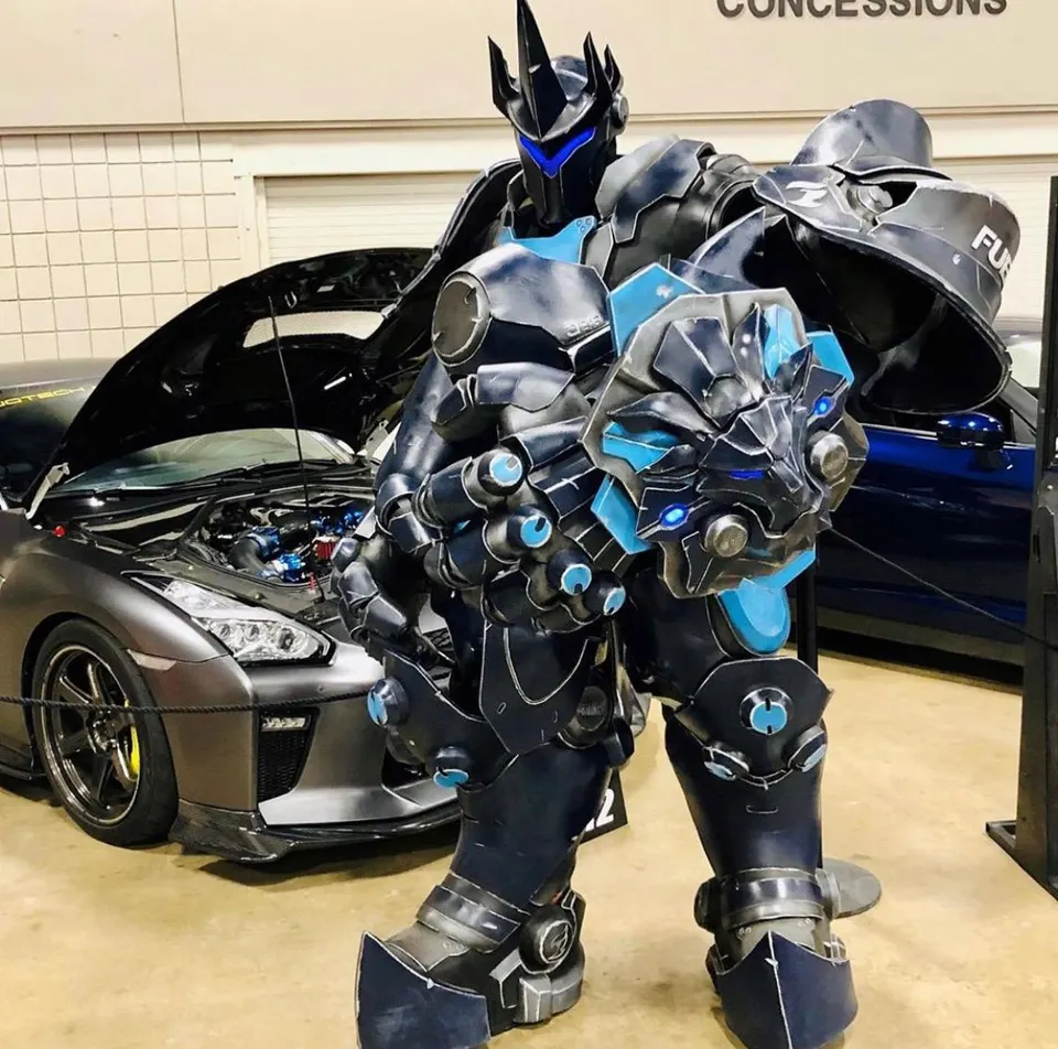 A person in a futuristic robot costume stands in front of a grey Nissan GT-R with its hood open at a car show.
