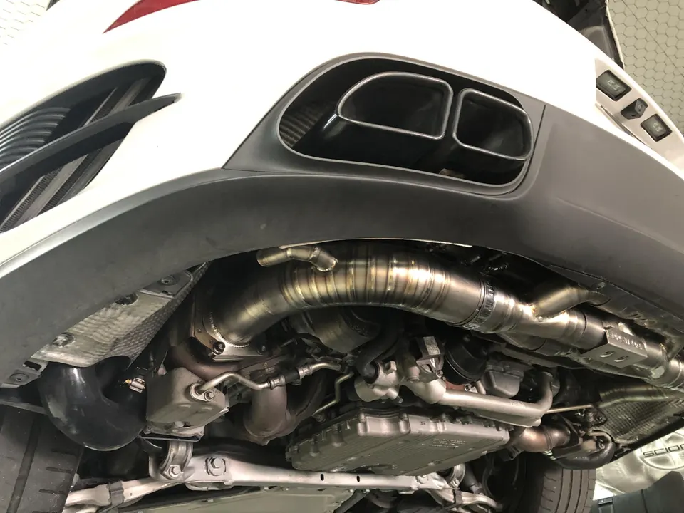 Close-up view of a performance titanium exhaust system and undercarriage components on a white Mercedes-AMG.