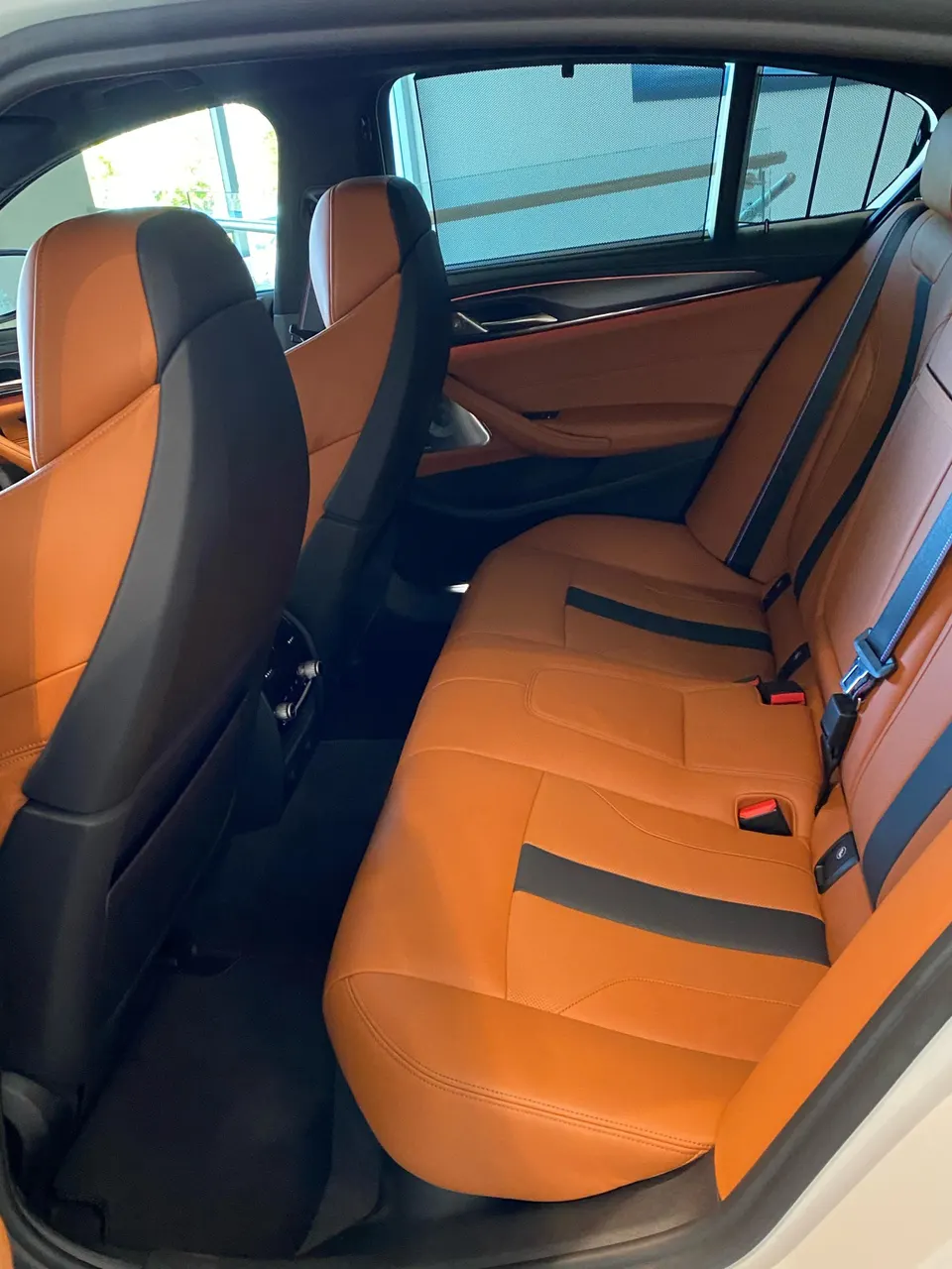 Rear interior of a luxury car featuring orange and black leather seats with ambient lighting on the door panels.