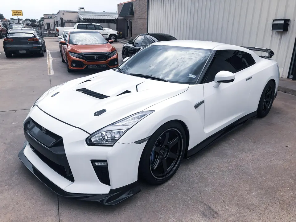 White Nissan GT-R with carbon fiber aero kit, aftermarket wheels, and vented hood parked outdoors.