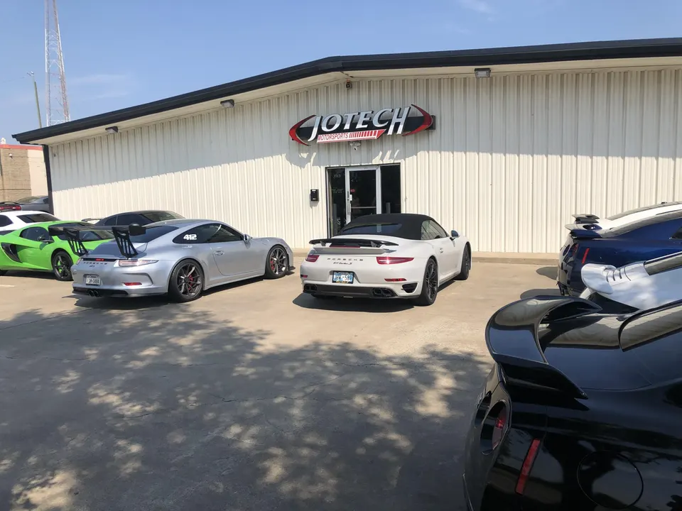 High-performance cars including Porsche 911 GT3, McLaren, and Nissan GT-R parked outside Jotech Motorsports shop.
