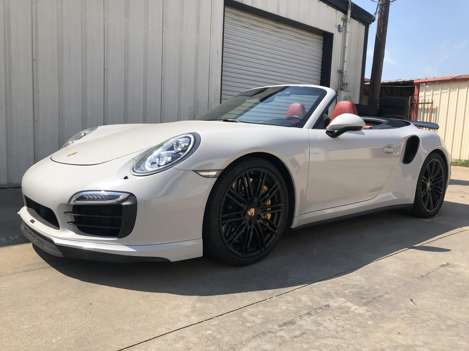A white Porsche 911 convertible with black wheels and red interior parked outside a building on a sunny day.