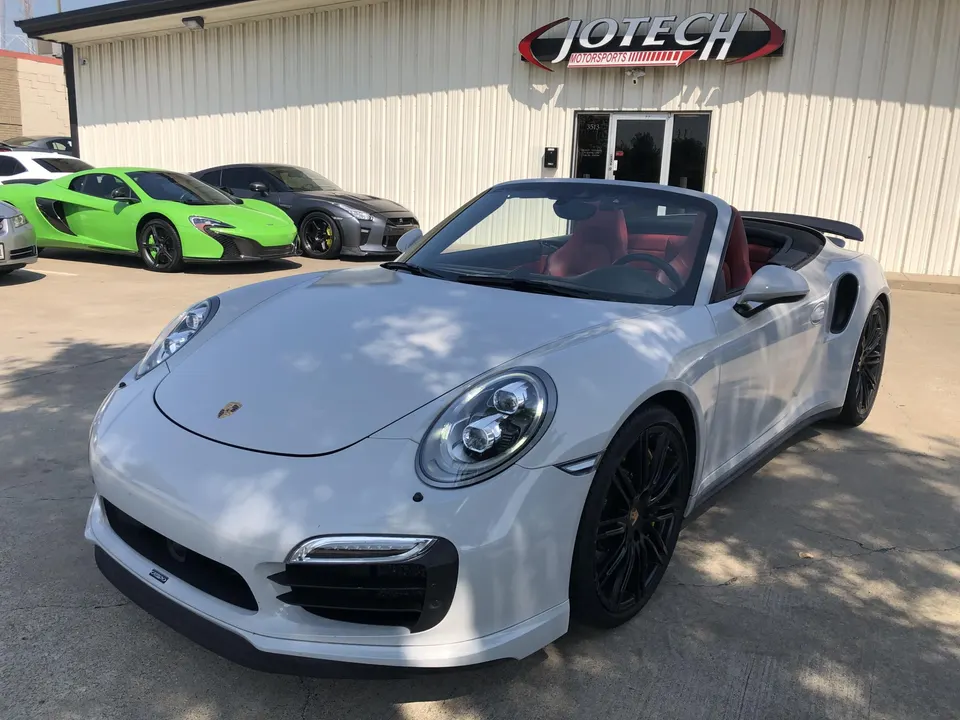 A white Porsche 911 convertible, a green McLaren, and a grey Nissan GT-R parked outside Jotech Motorsports.