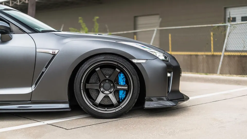 Close-up of a matte grey Nissan GT-R R35 with Volk Racing TE37 wheels, blue brake calipers, and carbon fiber aero.