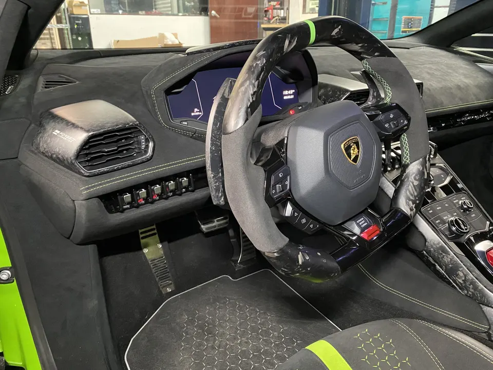A detailed view of the Lamborghini Huracan interior, featuring a carbon fiber steering wheel, alcantara dashboard, and sport pedals.
