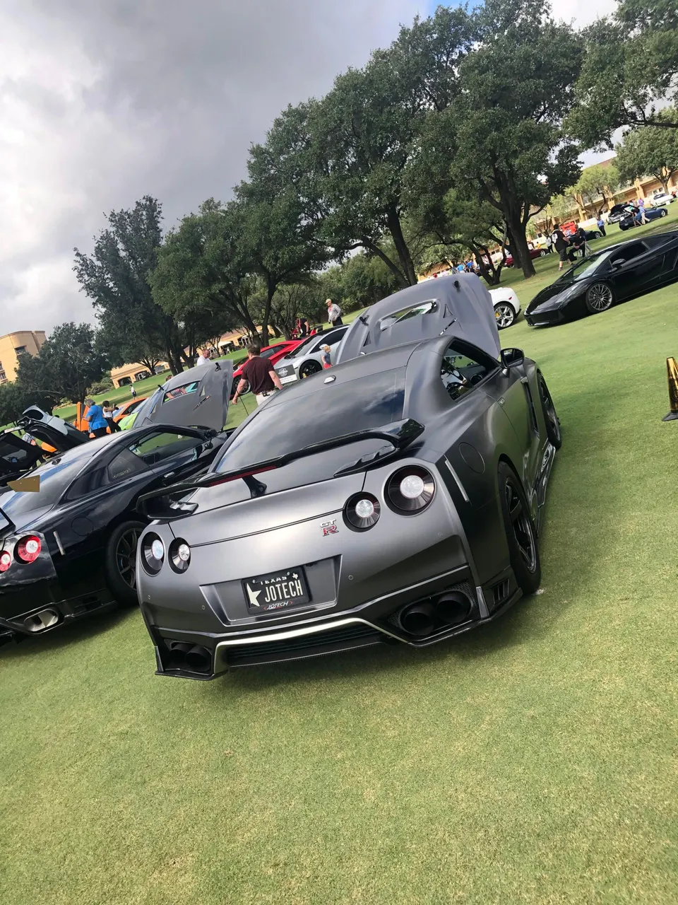 Multiple modified Nissan GT-Rs and other supercars displayed on a grassy field at an outdoor car show event.