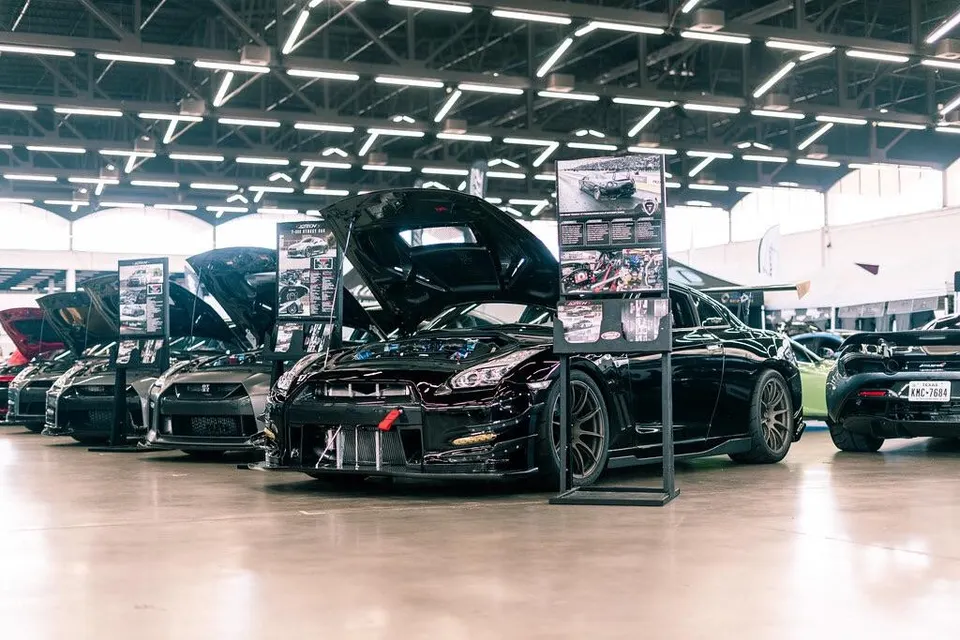 Multiple modified Nissan GT-Rs and other performance cars displayed at an indoor car show event with hoods open.