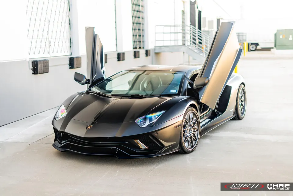 Black Lamborghini Aventador with scissor doors open, parked in a modern architectural setting.
