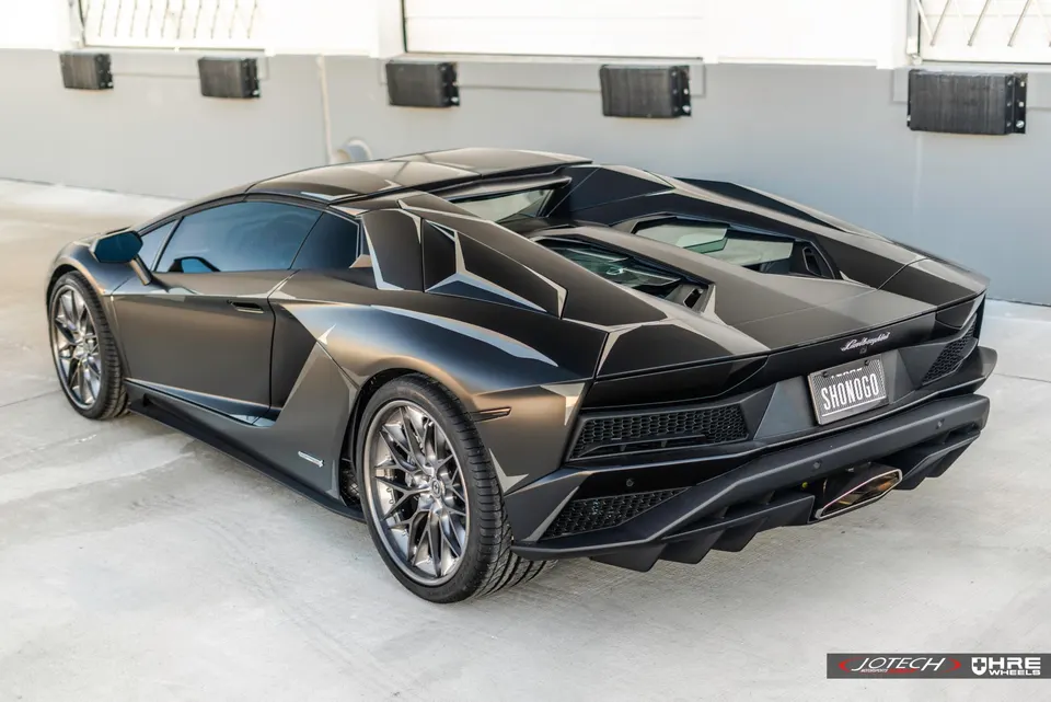 A black Lamborghini Aventador with custom wheels parked outdoors, showcasing its sleek design.