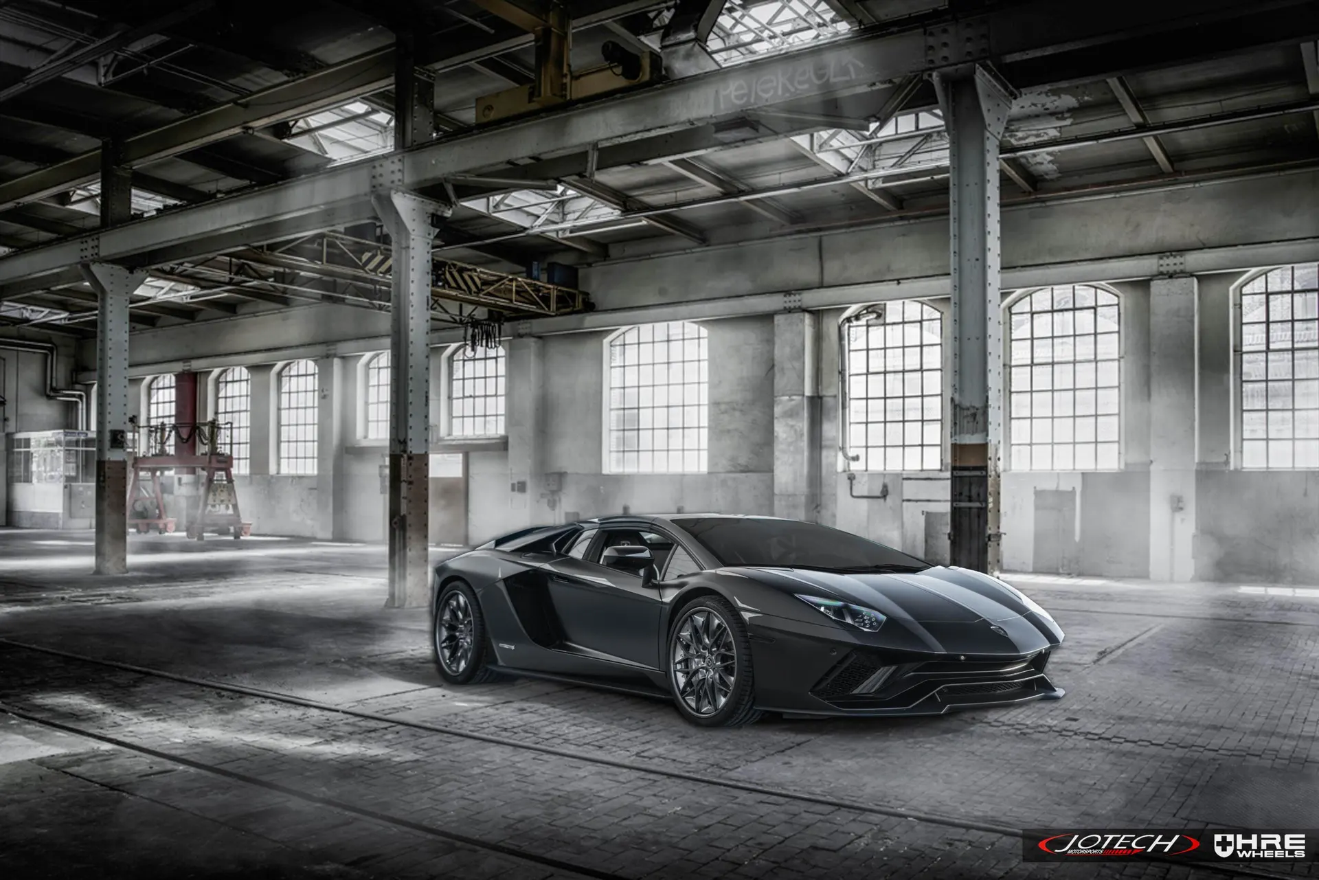 A grey Lamborghini Aventador supercar parked in a large, industrial warehouse with many windows.