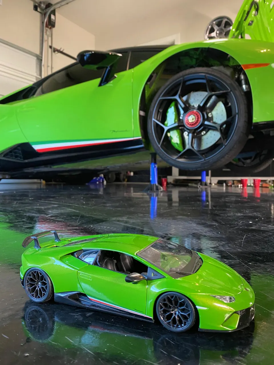 A green Lamborghini Huracan on a lift in a garage with a matching model car on the floor.