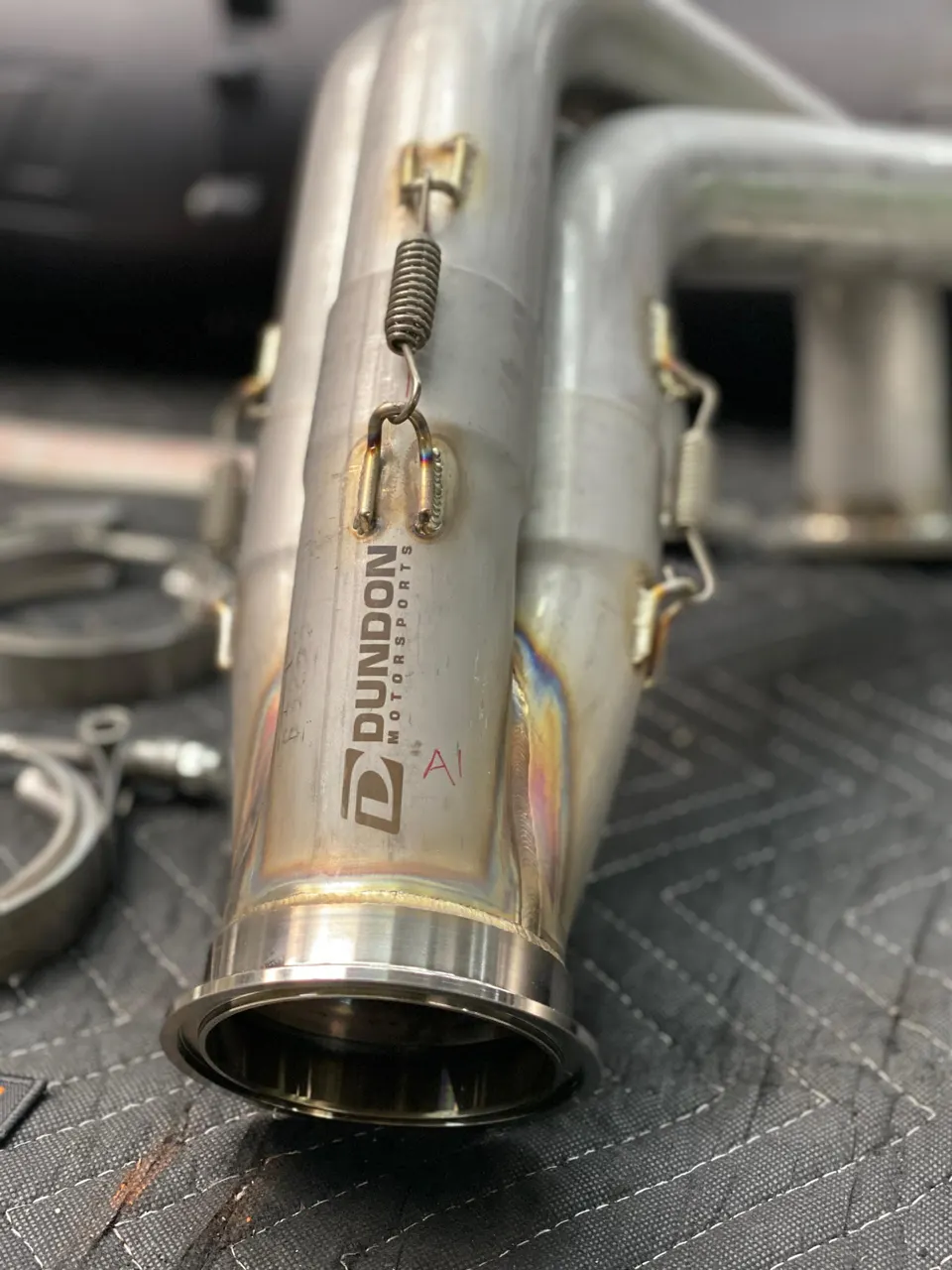 Close-up of a stainless steel Dundon Motorsports exhaust component with spring-loaded V-band clamp.