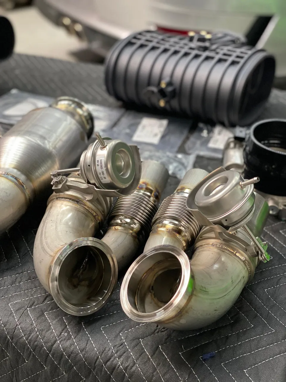 Performance exhaust components including downpipes with wastegate connections and a resonator, laid out in a shop.