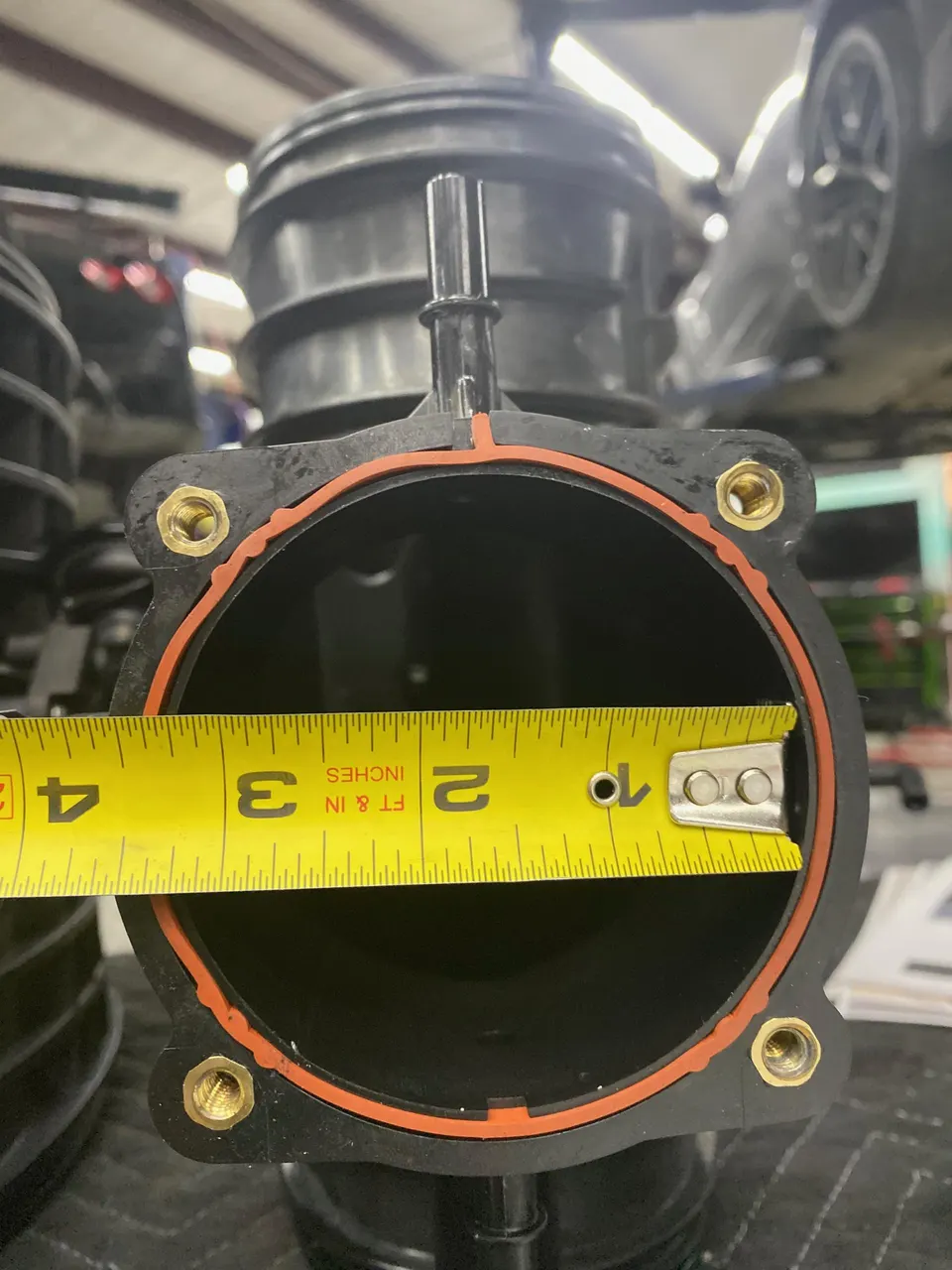 Close-up of an intake pipe or throttle body opening being measured with a tape measure in a performance shop.