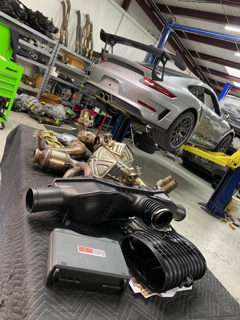 Porsche GT3RS on a lift in a shop with aftermarket exhaust and induction parts laid out on a table.