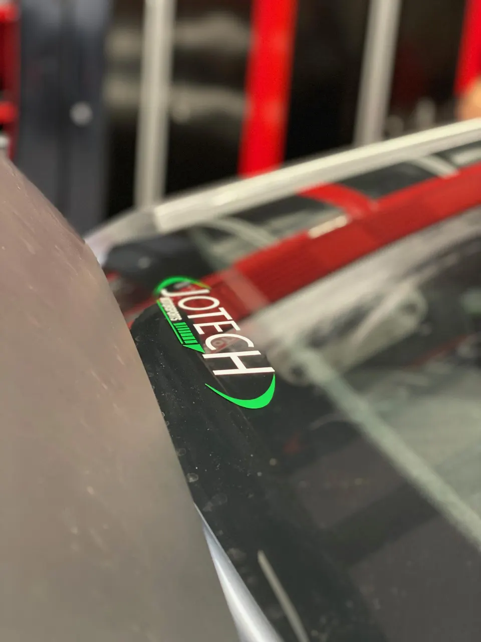 Close-up of a Jotech Motorsports sticker on the A-pillar of a performance car in a shop setting.