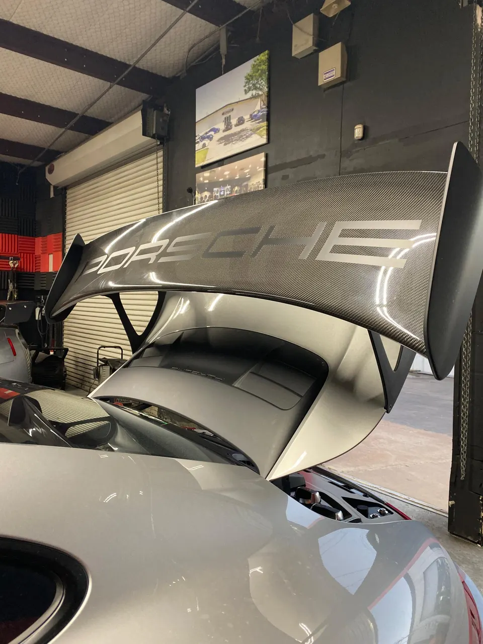 Rear view of a silver Porsche with a large carbon fiber wing in a performance shop.
