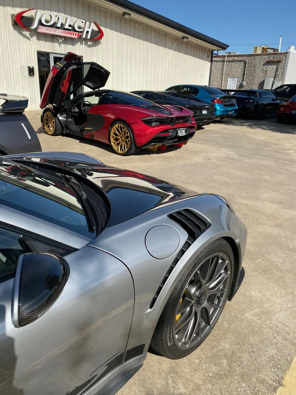 High-performance cars including a red McLaren and a grey Porsche parked outside Jotech Motorsports tuning shop.