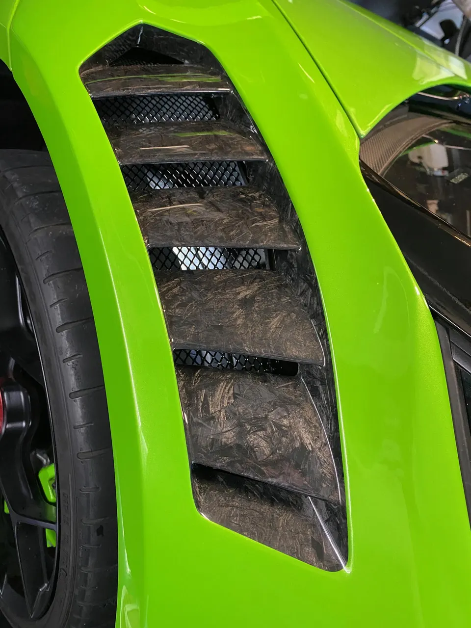 A close-up of a lime green supercar's fender with carbon fiber vents and a visible wheel and tire.