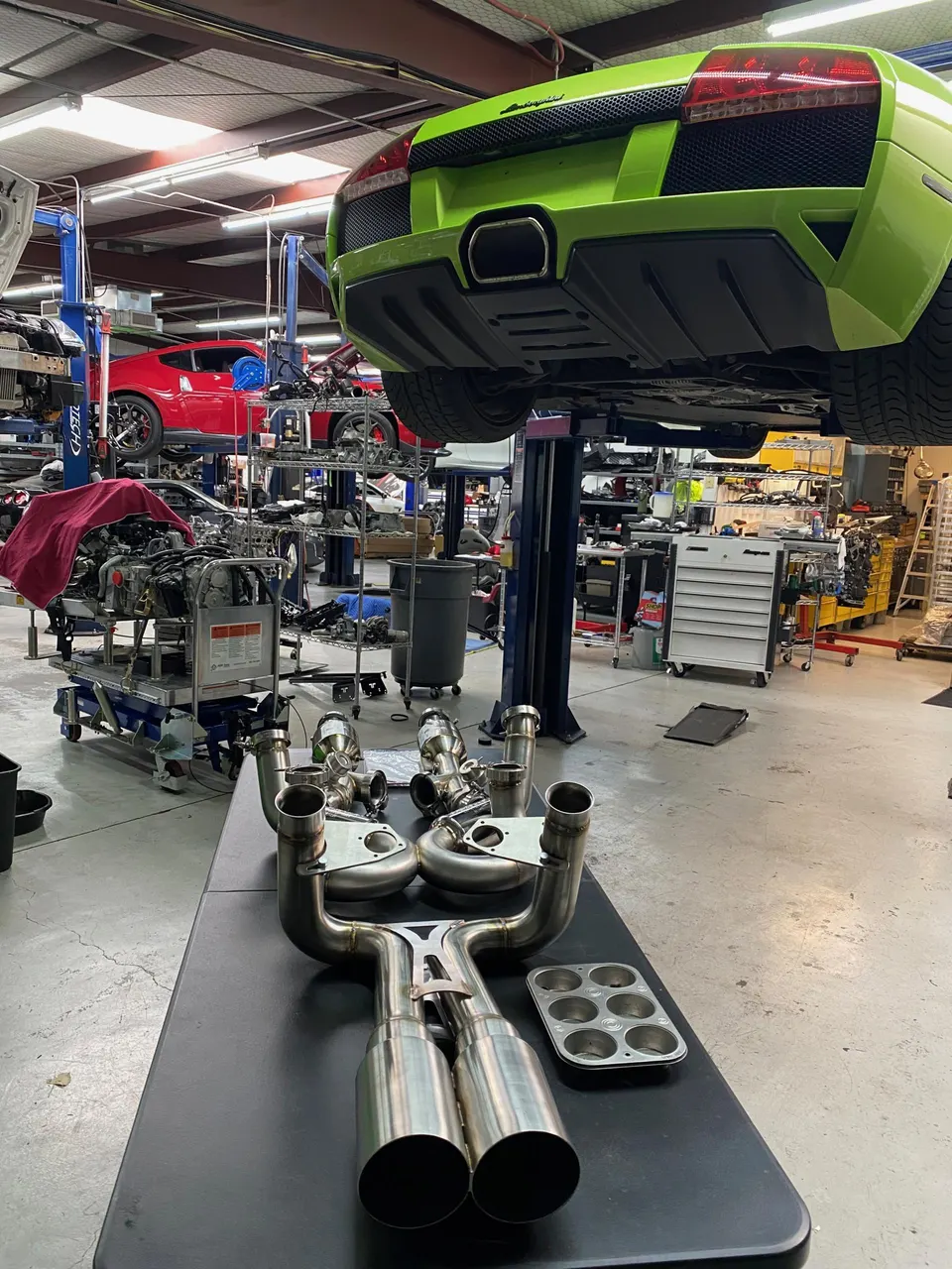 Green Lamborghini Murcielago on a lift in a performance shop with an aftermarket exhaust system on a table.