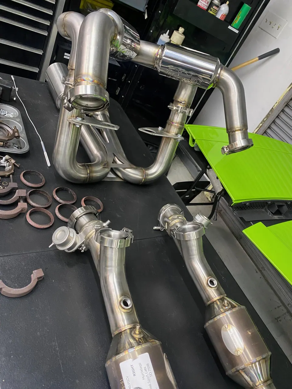 Stainless steel performance exhaust system components including headers and catalytic converters laid out on a workbench in a tuning shop.