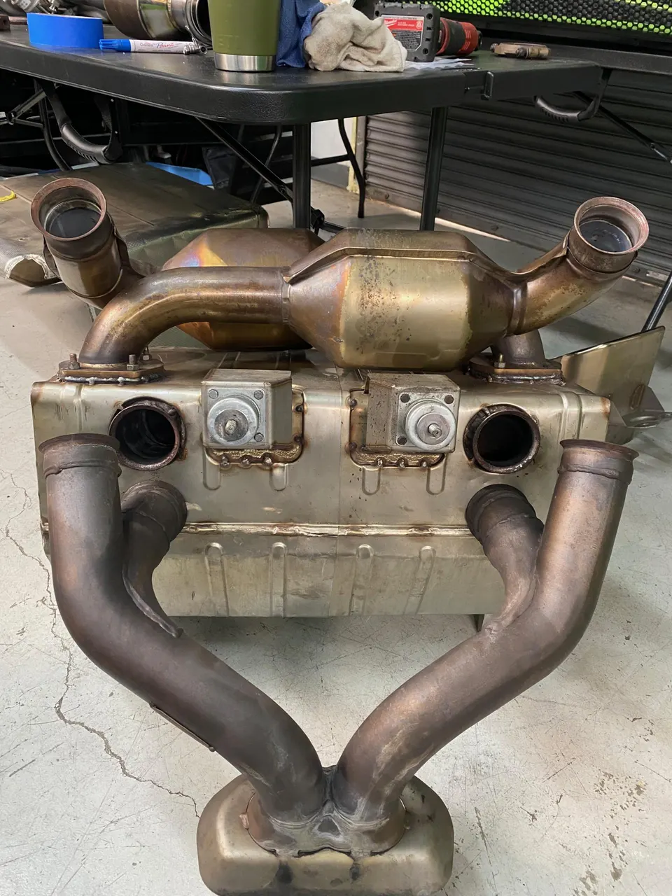 A used Porsche exhaust system with catalytic converters and mufflers on a shop floor, ready for installation or replacement.